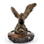 A plated metal car mascot modelled as an eagle, perched on a rocky base, on associated wood stand,