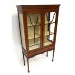 An Edwardian mahogany and inlaid display cabinet, with twin glazed doors above two shelves raised on