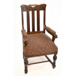 An early 20th century carved oak and upholstered elbow chair raised on turned and block front legs.