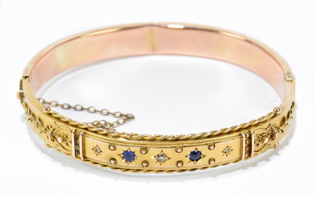 A 9ct yellow gold hinged snap bangle set with two small sapphire and three diamond chips to the