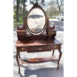 An Edwardian mahogany dressing table with oval mirror above a drawer and serpentine shelf on