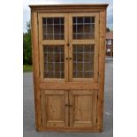 A pine freestanding corner cupboard, the moulded dentil cornice above leaded glazed upper doors