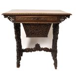 A 19th century Anglo-Indian profusely carved sewing table with a shallow compartmented drawer