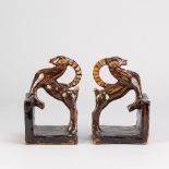 A pair of terracotta book ends modelled as horned animals covered in glossy glaze, incised MW marks,