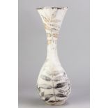 A tall smoke fired stoneware vessel with flared rim and compressed body covered in white glaze