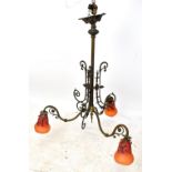 An Arts & Crafts style iron framed chandelier with scrolling mounts and four Schneider glass