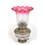 NEW ROCHESTER; an American silvered metal oil lamp with repousse decoration with clear cranberry