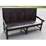 A Victorian carved oak settle in 18th century style, with five panel back above a solid seat on