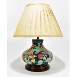 MOORCROFT; a modern baluster form table lamp with floral decoration on a green ground, on wooden