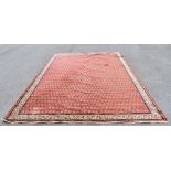 A Persian machine woven wool carpet, decorated with an all over Paisley design against a red ground,