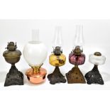 Four early 20th century oil lamps including an example with aubergine coloured glass reservoir,