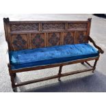 A 17th/18th century carved oak settle with panel back and upholstered seat on turned stretchered