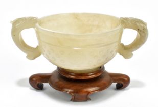 A Chinese carved and polished celadon jade twin handled cup, with central band of decoration to