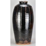 JIM MALONE (born 1946); a very tall fluted stoneware bottle covered in tenmoku breaking to kaki