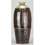 JIM MALONE (born 1946); a very tall part fluted stoneware bottle covered in tenmoku breaking to kaki