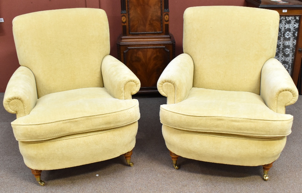 A pair of good quality yellow upholstered armchairs on turned supports with brass castors.