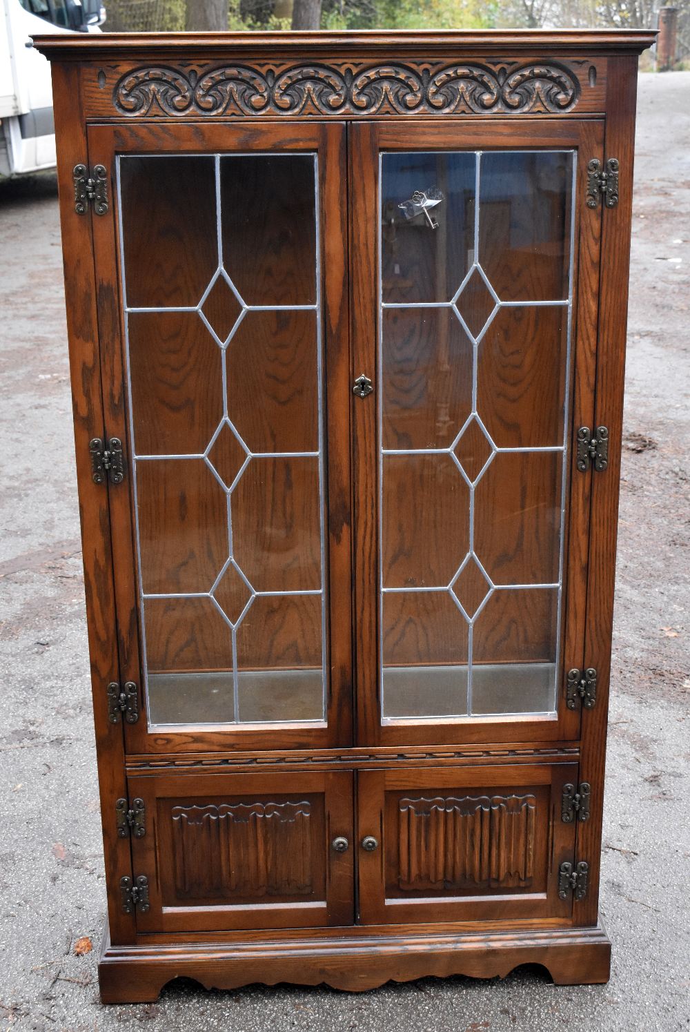 A modern Priory style oak display cabinet with carved detail and a pair of leaded glazed doors,