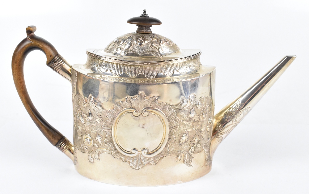 A George III hallmarked silver oval teapot, with embossed floral and scroll detailing, carved wood