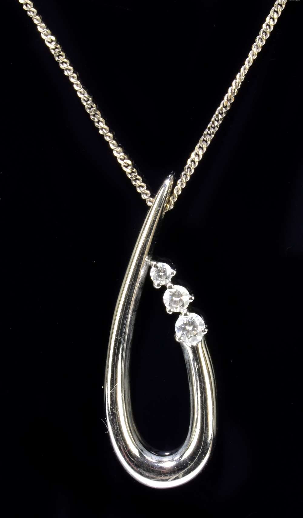 An 18ct white gold fine link chain suspending a swept white metal pendant set with three graduated