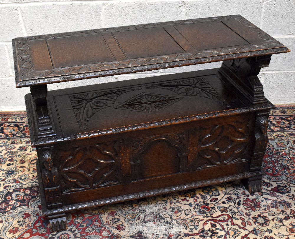 A 1920s carved oak monk's bench with carved and panelled back above the hinged seat, width 107cm,