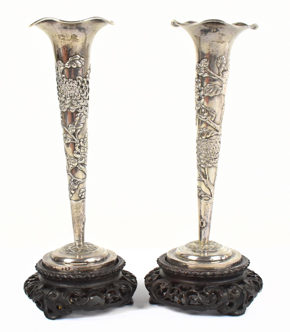 A pair of Chinese white metal vases with shaped rim and embossed tapering central column with floral