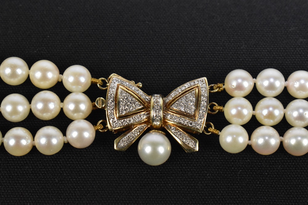 A three row Akoya pearl choker, with a yellow metal diamond set bow clasp, surmounting a single - Image 2 of 2