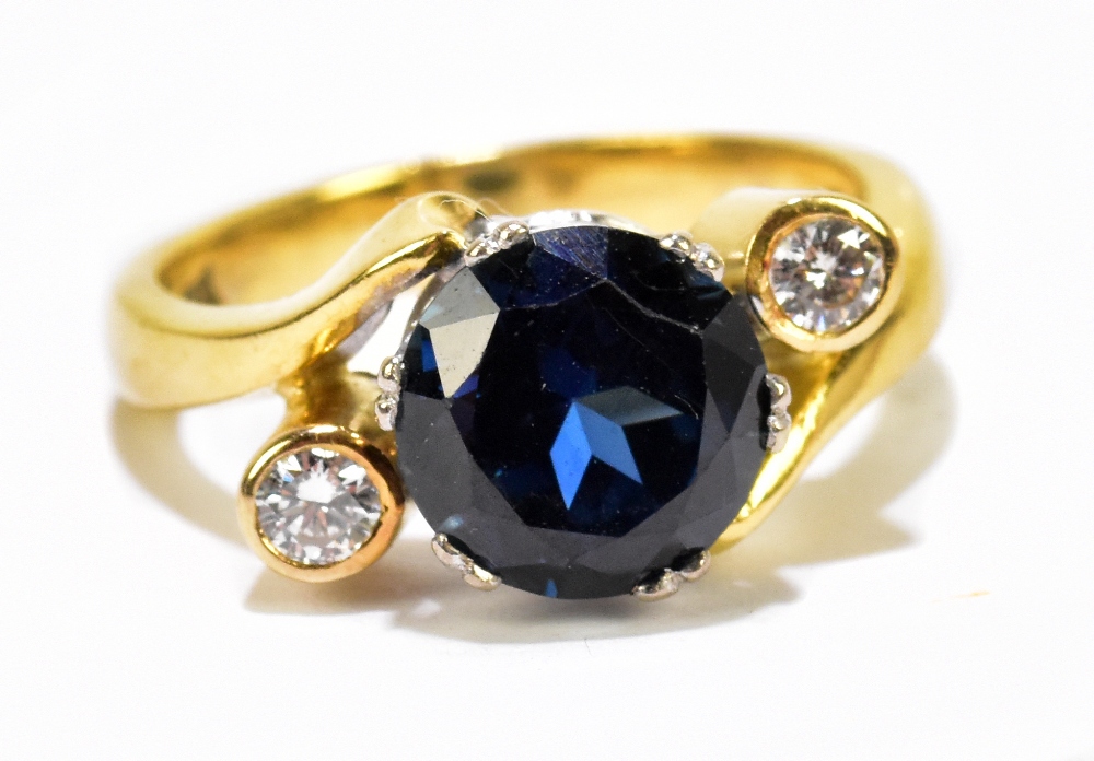 An 18ct yellow metal sapphire and diamond three stone ring, the circular sapphire flanked by