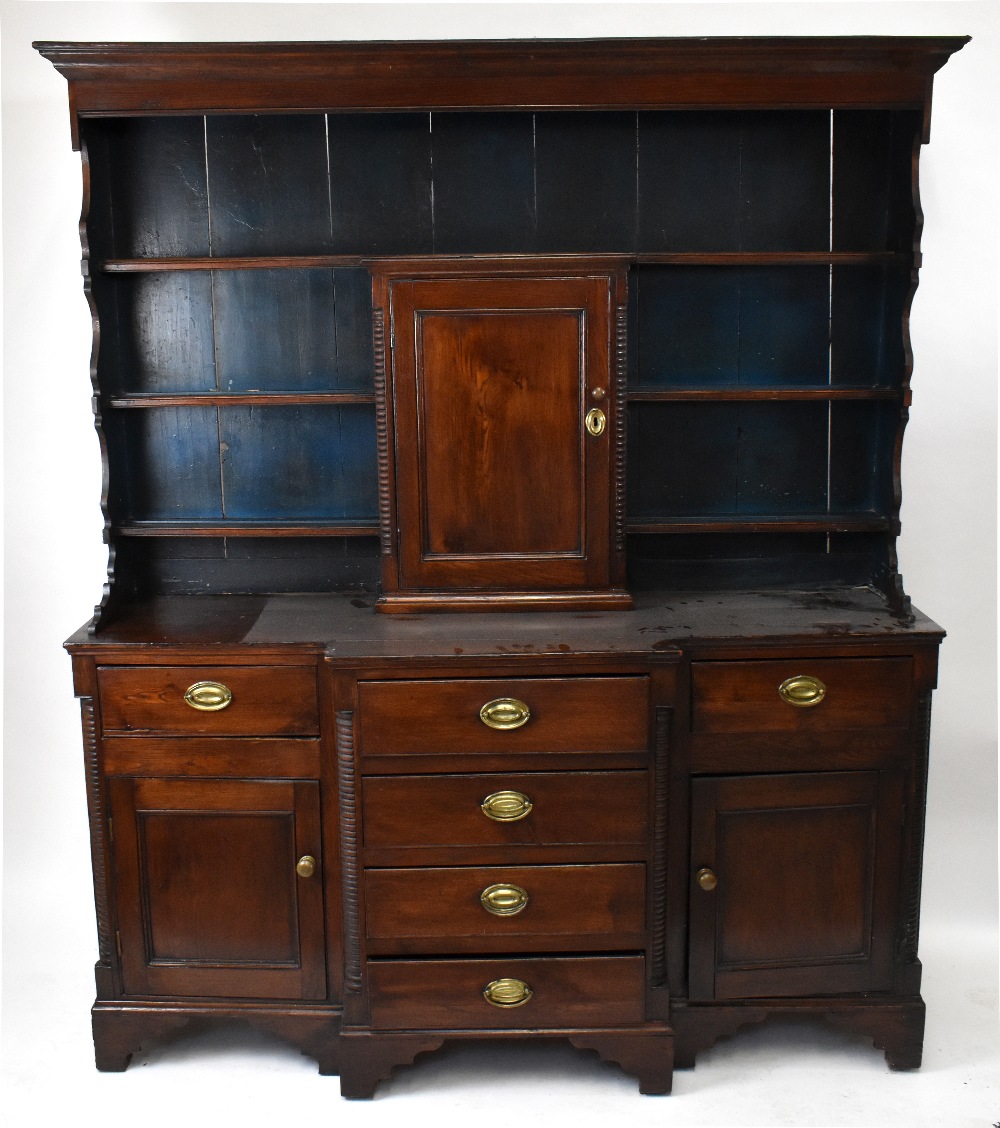 A late 18th/early 19th century oak breakfront dresser, the boarded back with three fixed shelves and