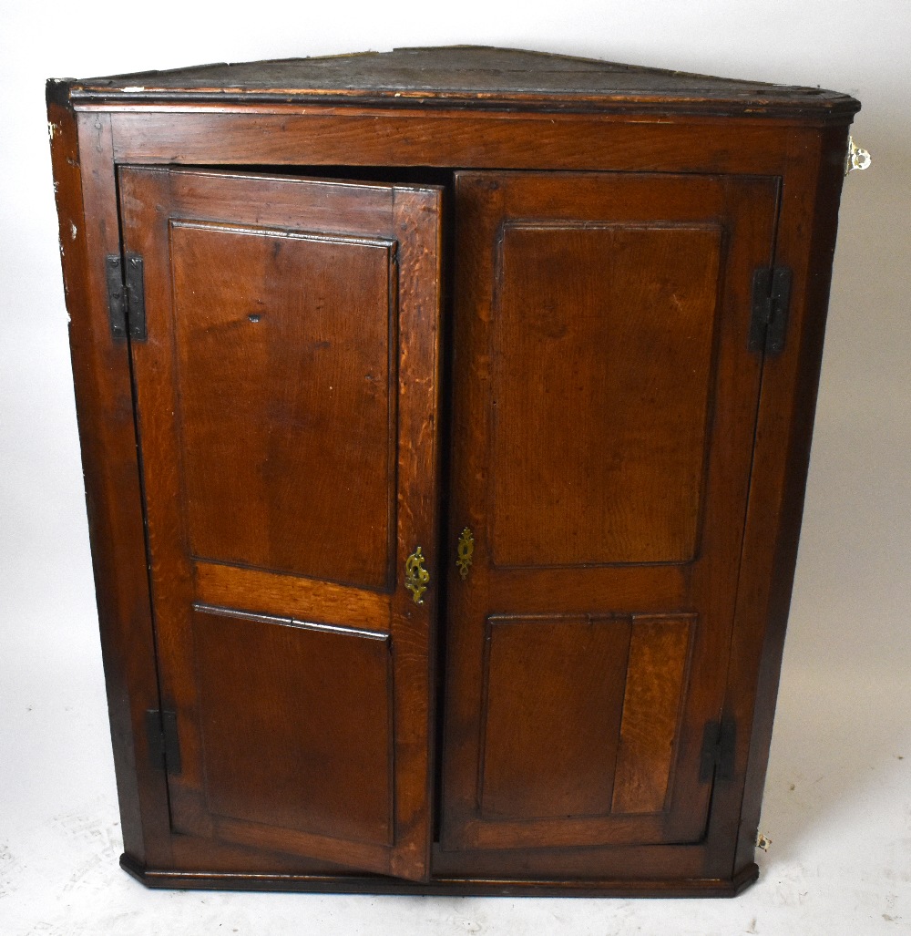 An 18th century oak hanging corner cupboard with iron H-hinges and a pair of panelled doors, width