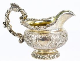 A George IV hallmarked silver cream jug with ornate scroll handle and embossed main body decorated