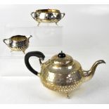 A George V hallmarked silver three-piece tea set of bulbous form with planished finish,