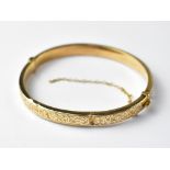 A ladies' vintage 9ct gold hinged bracelet with floral pattern to one half, the other half blank,