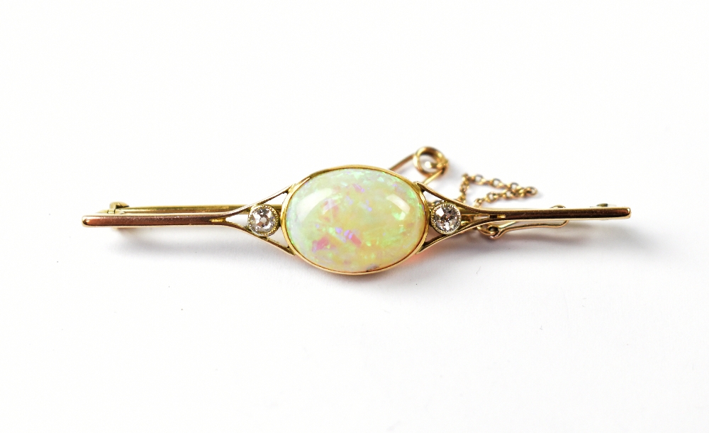 A yellow metal bar brooch set with central opal flanked by two diamonds, with safety chain.