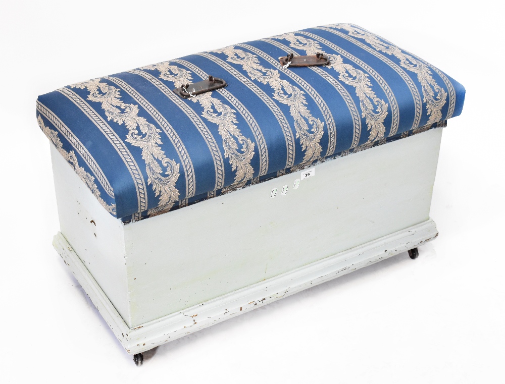 A pale blue painted pine ottoman with upholstered hinged lid, raised on castors, 56 x 90 x 47cm.