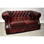 PEGASUS; an oxblood leather button pressed two-seater Chesterfield-style settee, raised on bun feet.