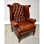 A reproduction dark tan leather button pressed and stud decorated wingback armchair,