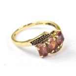 A modern 9ct gold crossover ring, with three inset pink stones with rainbow hue,
