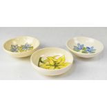 MOORCROFT; three shallow bowls, one with a yellow lily, the others with periwinkle-style decoration,