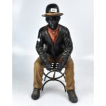 A decorative fibreglass figure of a seated gentleman upon a chair.