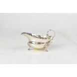 A George V hallmarked silver small sauce boat with serrated patterned edge, C-scroll handle,