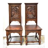 A pair of late Victorian carved oak hall chairs, each panelled back decorated with a stork,