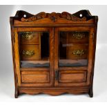 An Edwardian smoker's cabinet with twin glazed and panelled doors enclosing a central well and four