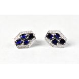 A pair of modern earrings with four claw set blue sapphires in a border of channel set tiny