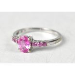 A 9ct white gold ring with central claw set cut oval pink sapphire flanked by three smaller claw