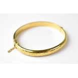 A 9ct gold hinged bracelet with floral chased pattern, with safety chain, approx 10.7g.