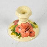 MOORCROFT; a cream ground squat candlestick with orange tube lined 'Hibiscus' pattern, height 9cm.