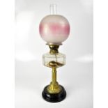 A brass oil lamp with chimney and acid etched rose tinted globular shade, above a glass reservoir,