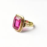 A yellow metal and synthetic pink stone ring, size O1/2, the head 18 x 15mm, approx 7.6g.