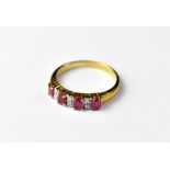 A 9ct gold ruby and diamond ring with four claw set oval rubies separated by three rows of two tiny