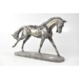 A white metal model of a horse with saddle, on a stylised grassy oval plinth base,